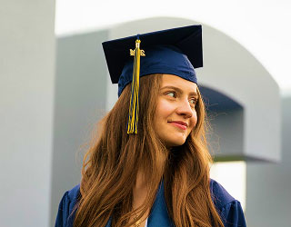 Graduada con birrete alt="Joven con toga y birrete de graduación mirando hacia un lado"