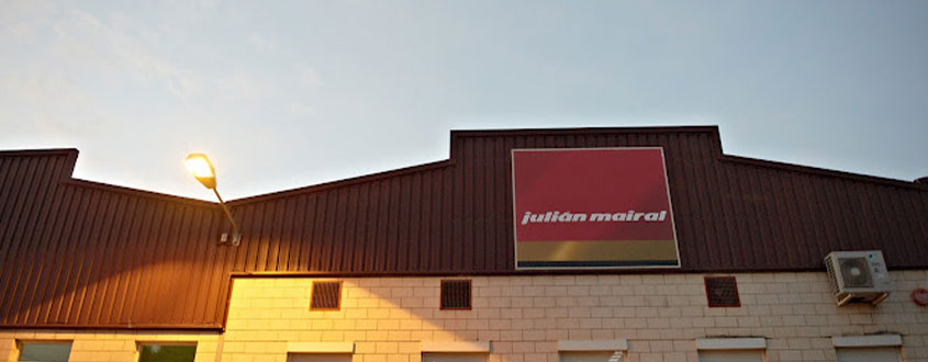 alt="Fachada exterior de una nave industrial con el rótulo de la empresa Julián Mairal al atardecer."